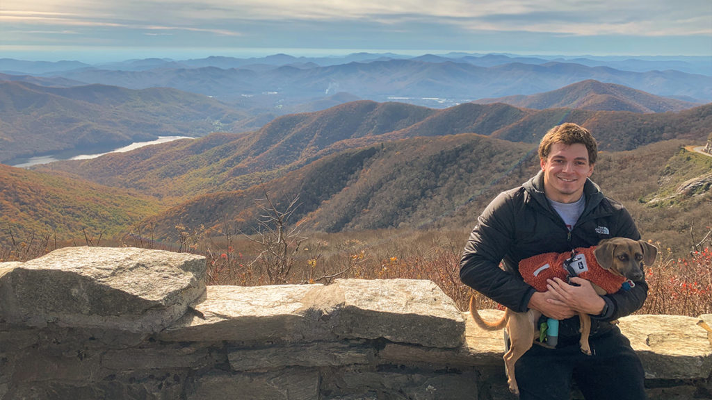 Ben holding his dog Lola while sitting on a stone wall on a hike in North Caroline.