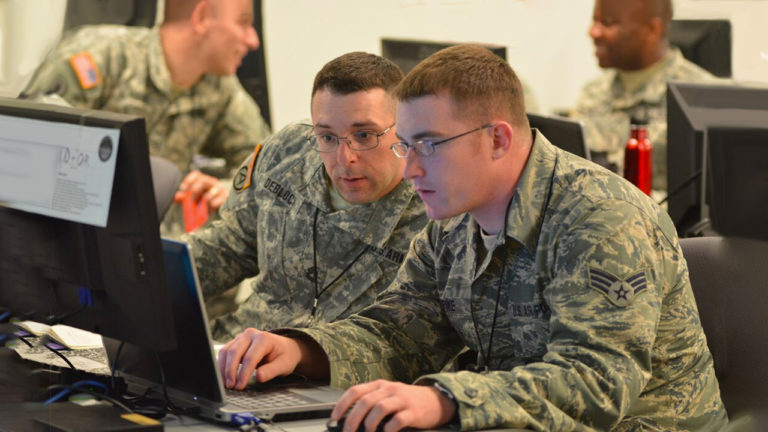 Two soldiers at a laptop discussing cyber shield exercise